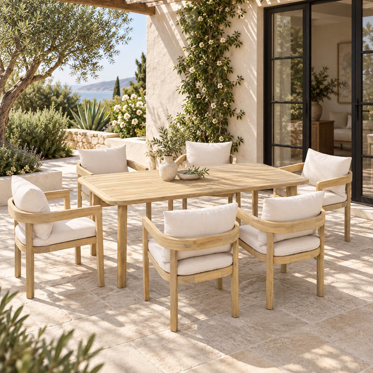 Leather Gallery Carenero Natural Ash Frame Oatmeal Dining Set, featuring a light wood outdoor dining table and six matching cushioned armchairs on a stone patio.