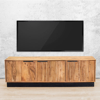 Gallery Everyday Lazlo TV Stand - 1.75m, featuring warm wood grain, vertical slat detailing, black handles, and a black base beneath a wall-mounted TV.